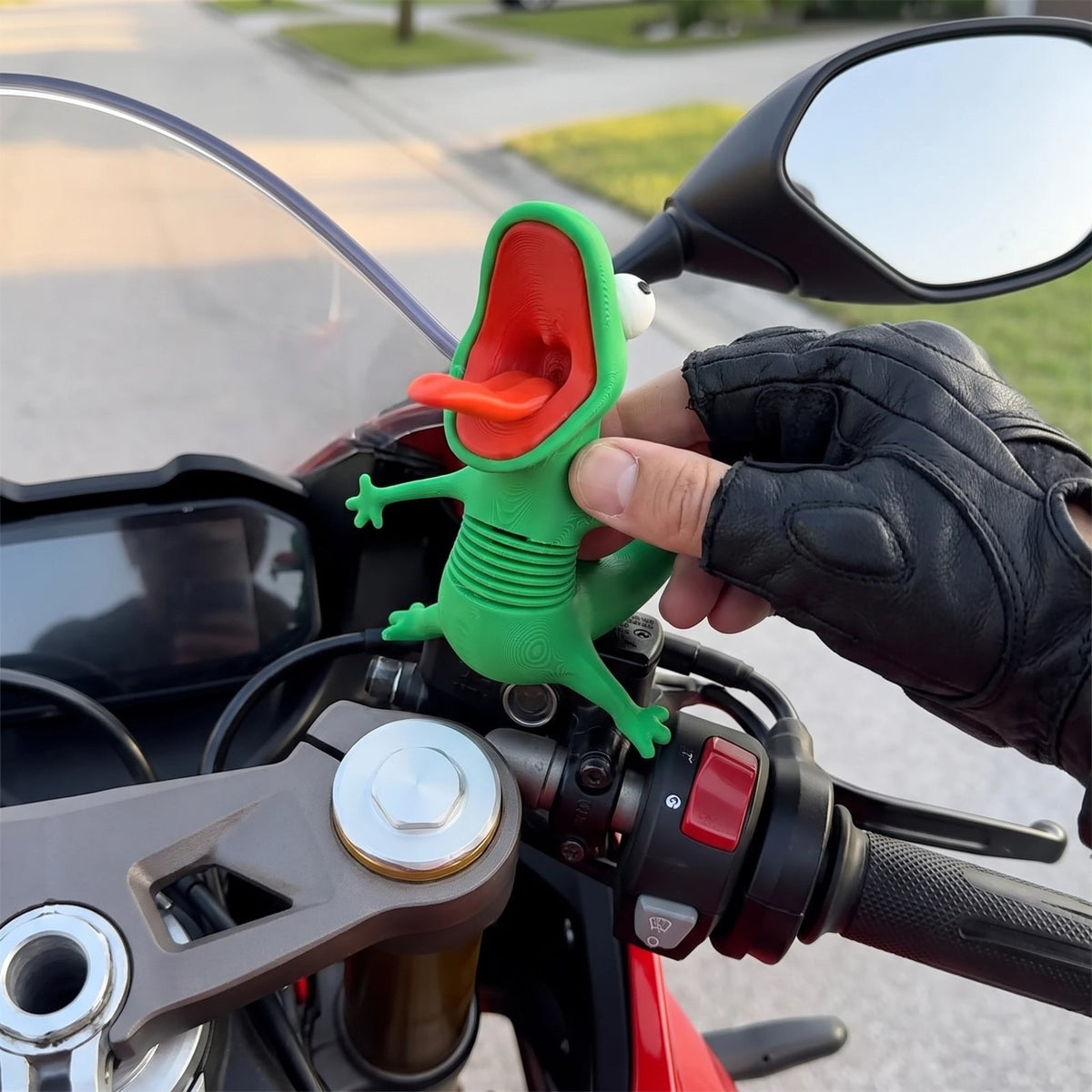 Rider pressing the green lizard figure onto a motorcycle next to the handlebar